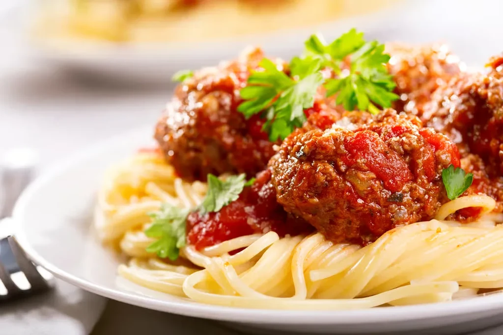 Plate of spaghetti and meatballs with red sauce, parsley, and cheese.