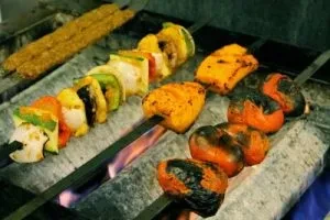 Meat kebabs and charred vegetable skewers grilling over open flames.
