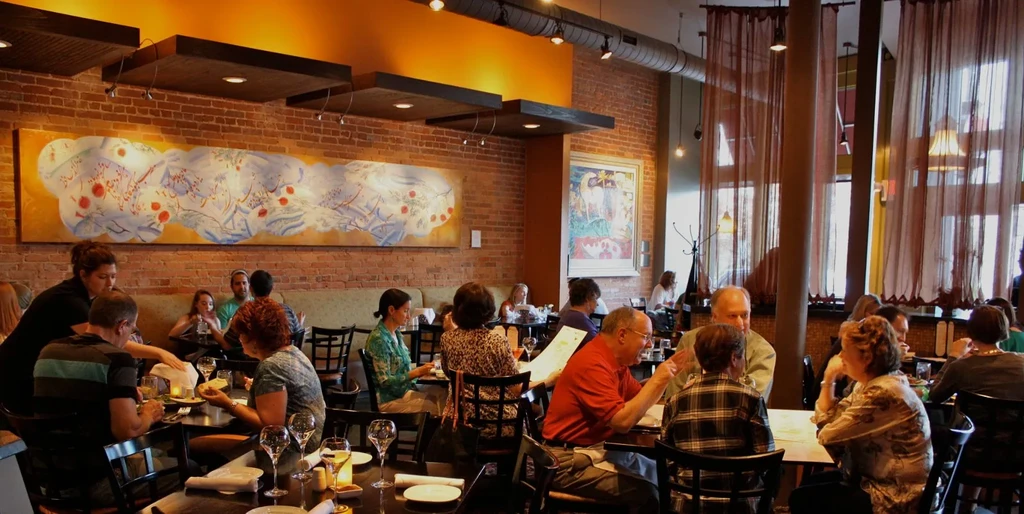 Bustling restaurant with diners, exposed brick, colorful art, and industrial ceiling.