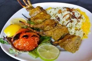 Grilled lamb chops, saffron rice, grilled tomato, and lemon wedges.