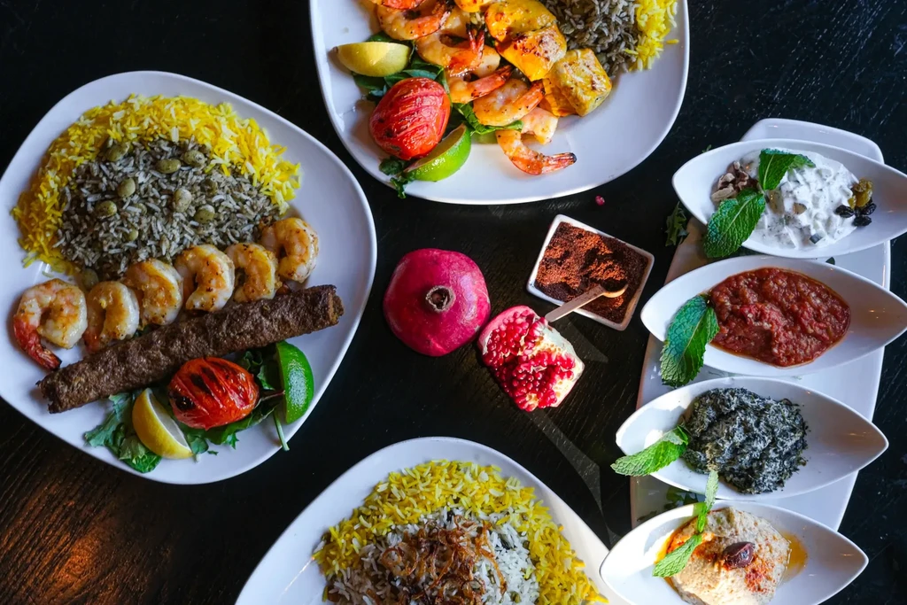 Overhead spread of Middle Eastern kebabs, chicken, shrimp, rice, pomegranate, dips.