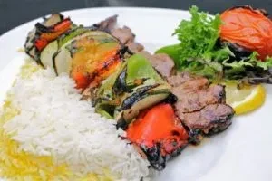 Grilled meat and vegetable skewer, rice, tomato, and lemon.