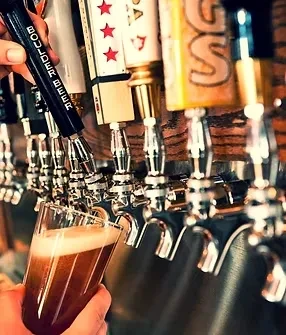 Hand pours dark beer from bar tap into a pint glass.
