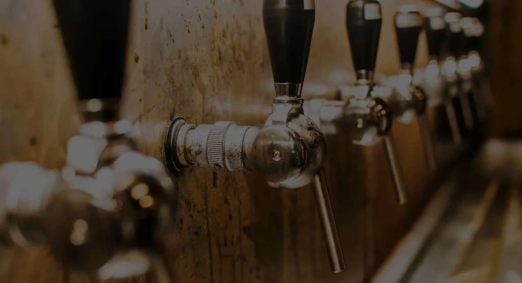 Dimly lit close-up of shiny beer taps against a rustic wall.