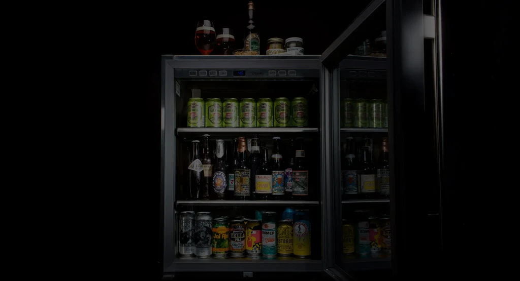 Brightly lit, open beverage cooler stocked with drinks, glasses, and jars.
