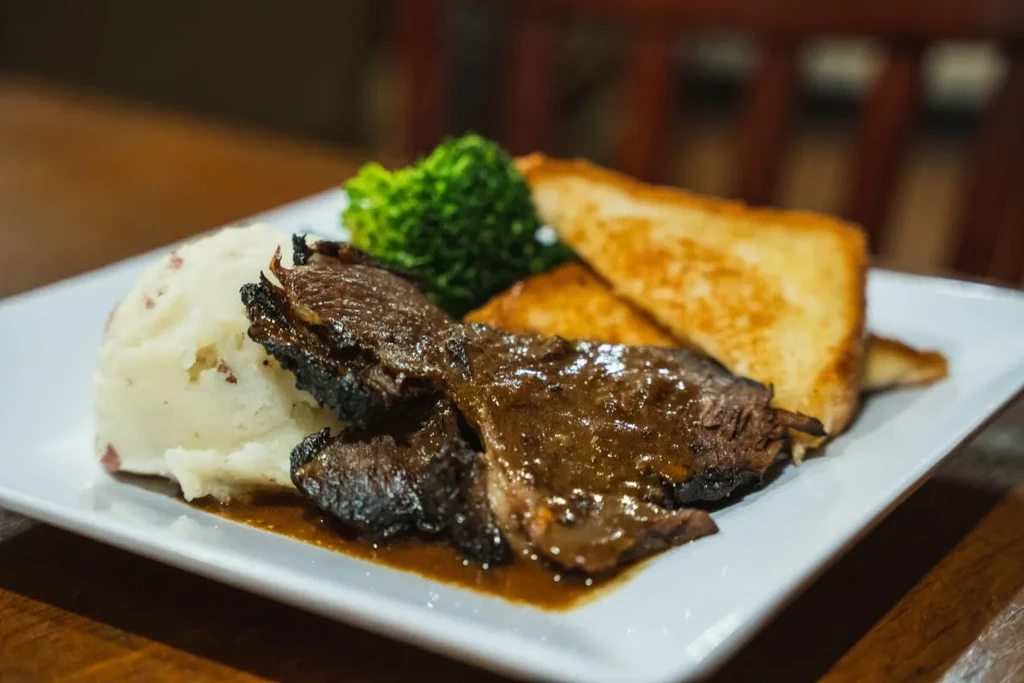 Plate with braised meat, mashed potatoes, broccoli, and thick-cut toast.