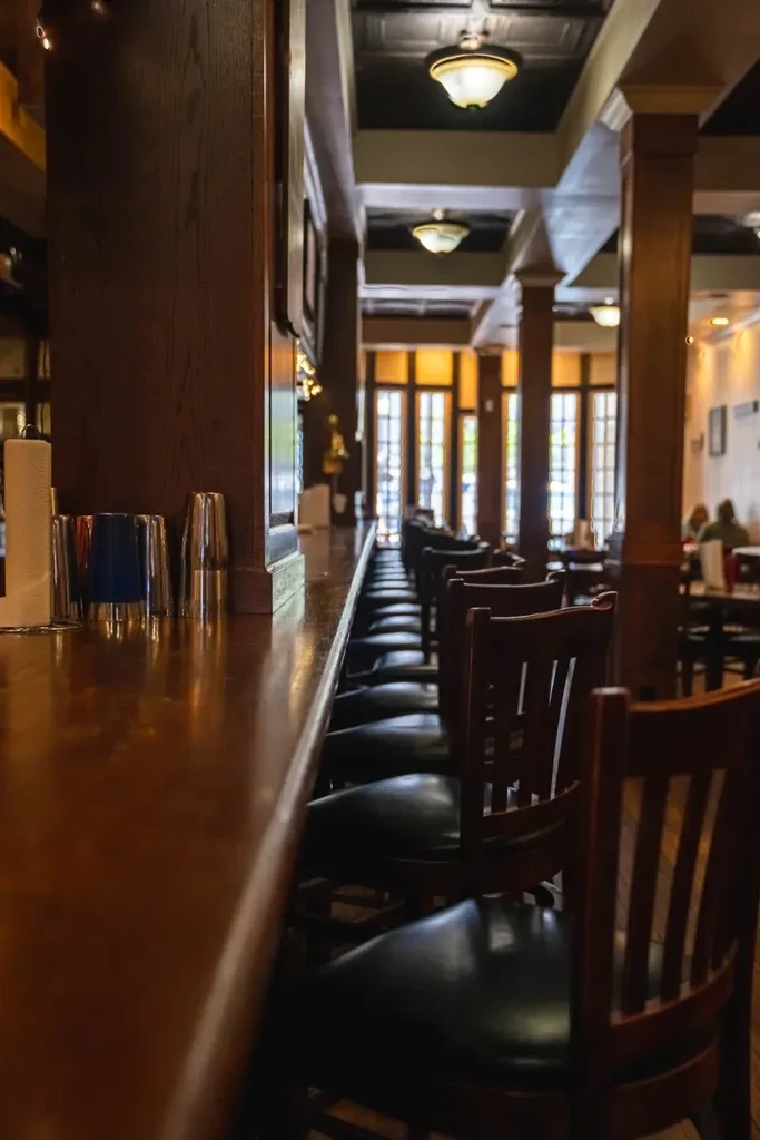 Warmly lit wooden bar with stools, cups, and dining area.