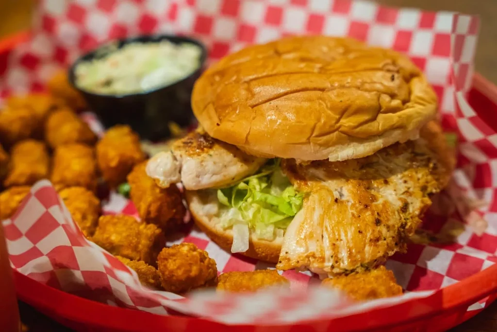 Close-up of chicken sandwich and tater tots in a red basket.