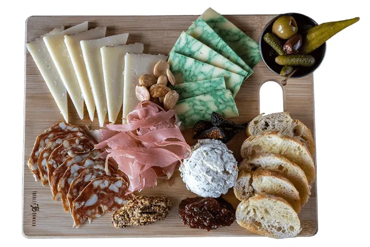 Charcuterie board with cheeses, cured meats, nuts, spreads, baguette, and olives.