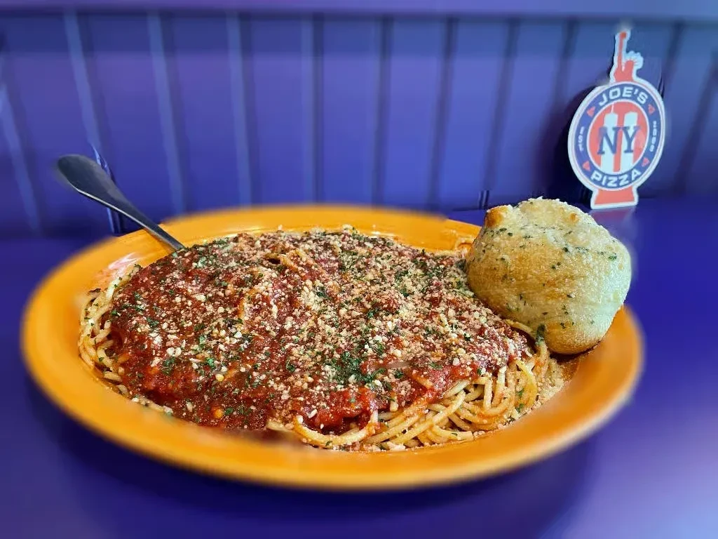 Plate of spaghetti with marinara, cheese, herbs, and a bread roll.