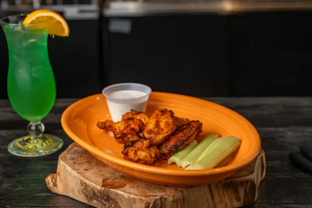 Orange plate of chicken wings, celery, dipping sauce, and green drink.