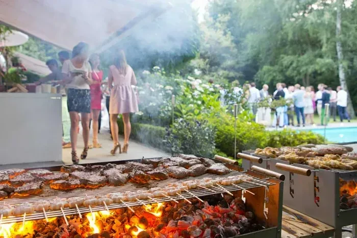 Two large grills cooking various meats outdoors, smoke rising.