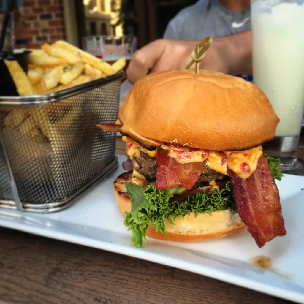Gourmet double burger with bacon, lettuce, orange sauce, and golden fries.