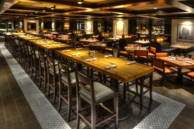 Warmly lit, unoccupied restaurant interior with high-top tables and booths.