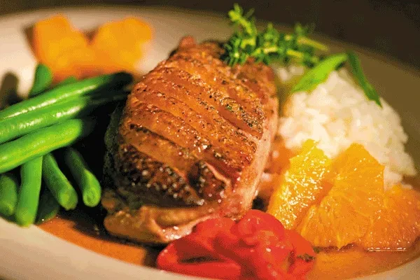 Plated seared meat with rice, string beans, orange, and red peppers.