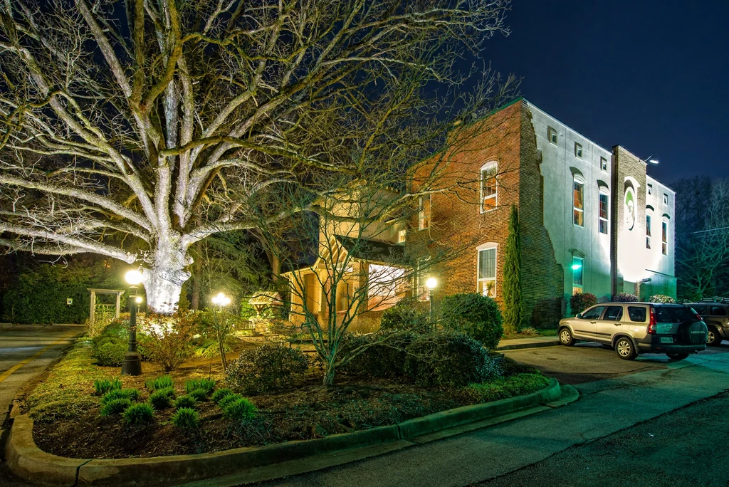 Night photo: lit brick building, bare tree, art, and landscaped garden.