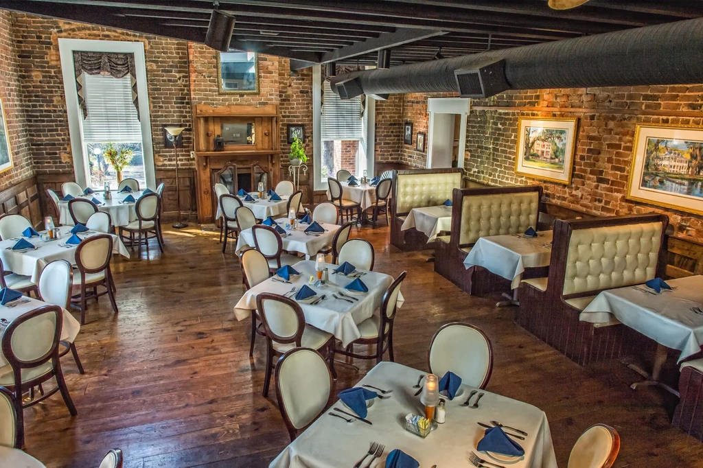 Empty upscale dining room with brick walls, fireplace, and set tables.