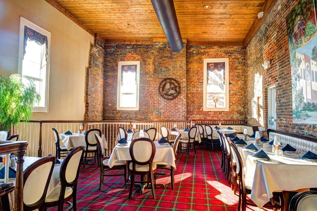 Rustic yet elegant restaurant interior with brick walls, wooden ceiling, plaid carpet.