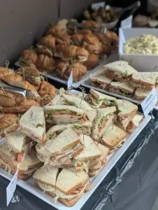 Display of assorted sandwiches, sliders, and creamy salad on a dark tablecloth.