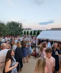 Crowded outdoor patio event at dusk with people socializing and drinking.