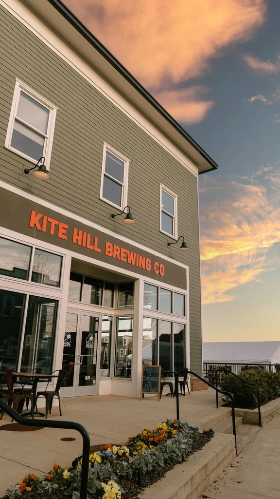 Kite Hill Brewing Co. building with patio, flowers, under sunset sky.