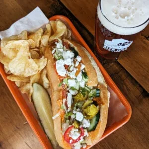 Sub sandwich, chips, pickle, and beer on an orange tray.