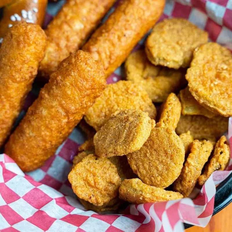 Golden-brown fried mozzarella sticks and pickle chips in a checkered basket.