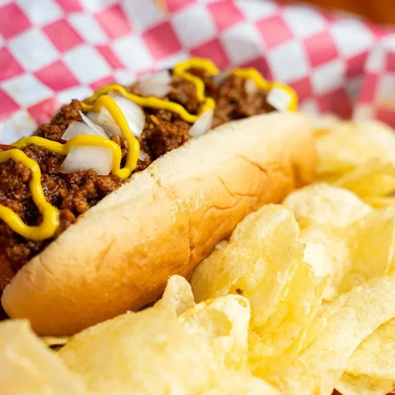 A chili dog with onions, mustard, and golden potato chips.