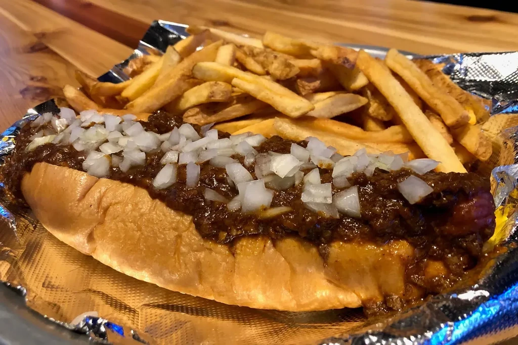 Close-up of a chili dog with diced onions and golden fries.