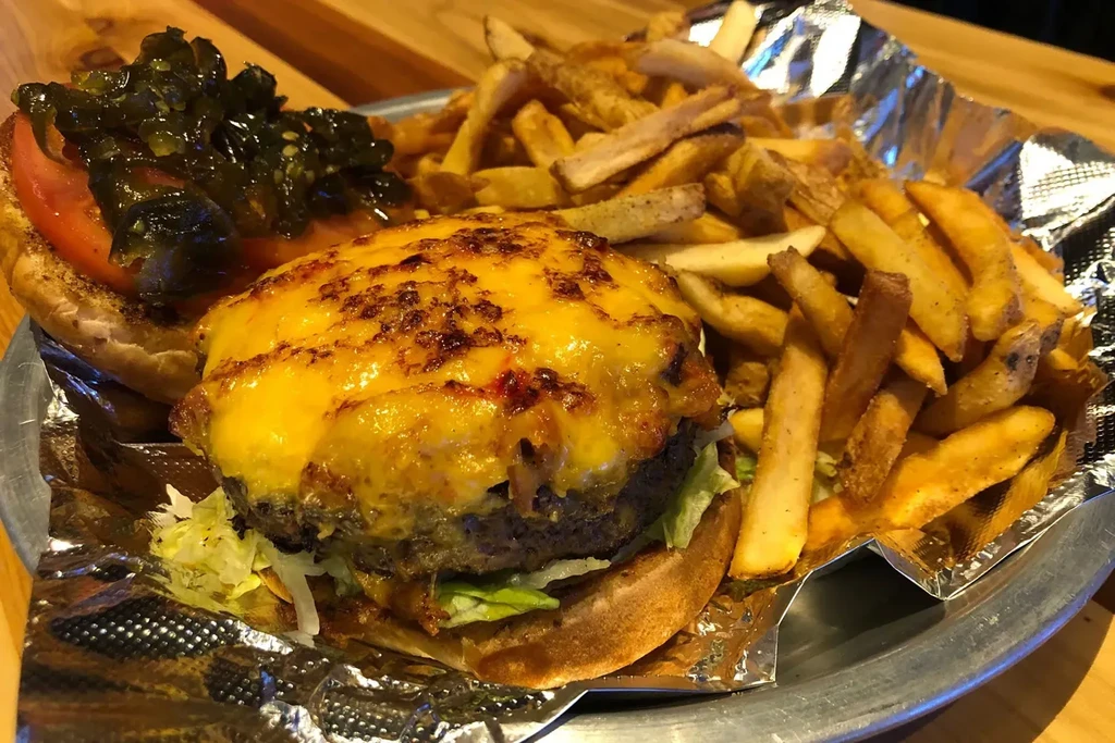 Close-up: Thick burger with melted cheese, lettuce, tomato, and rustic fries.