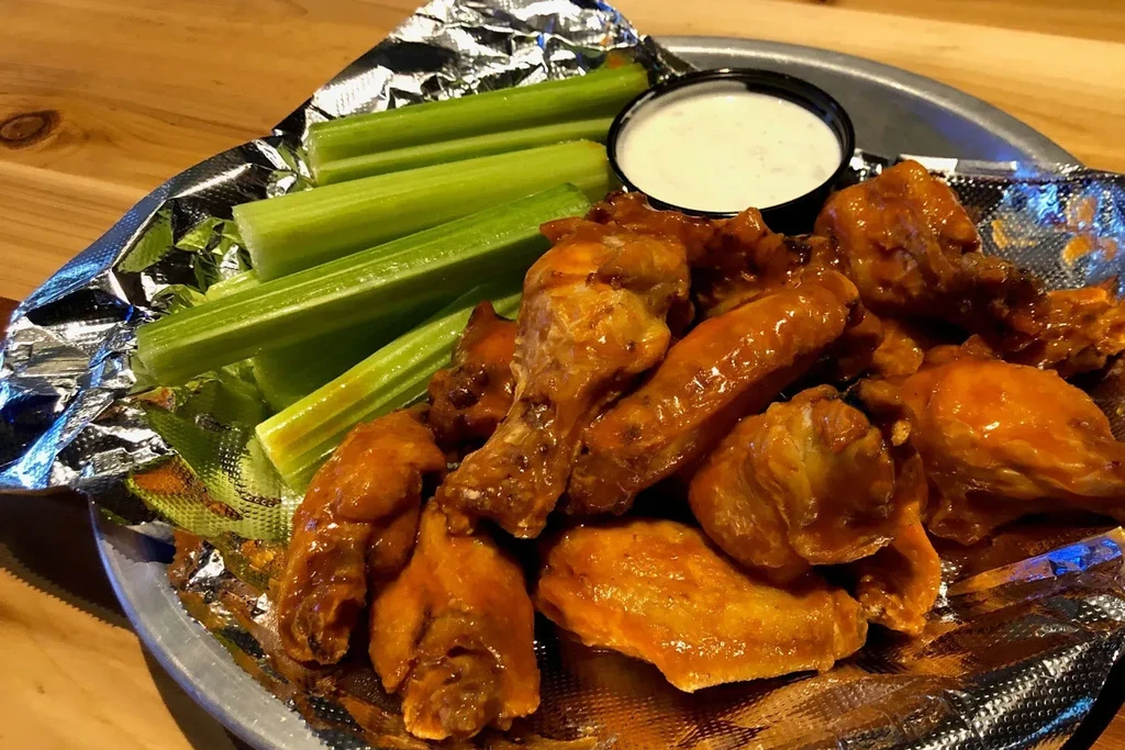 Buffalo chicken wings, celery sticks, and dip on a foil-lined plate.