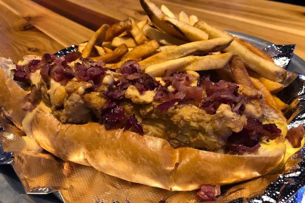 Chicken sandwich with red toppings, creamy sauce, and fries.