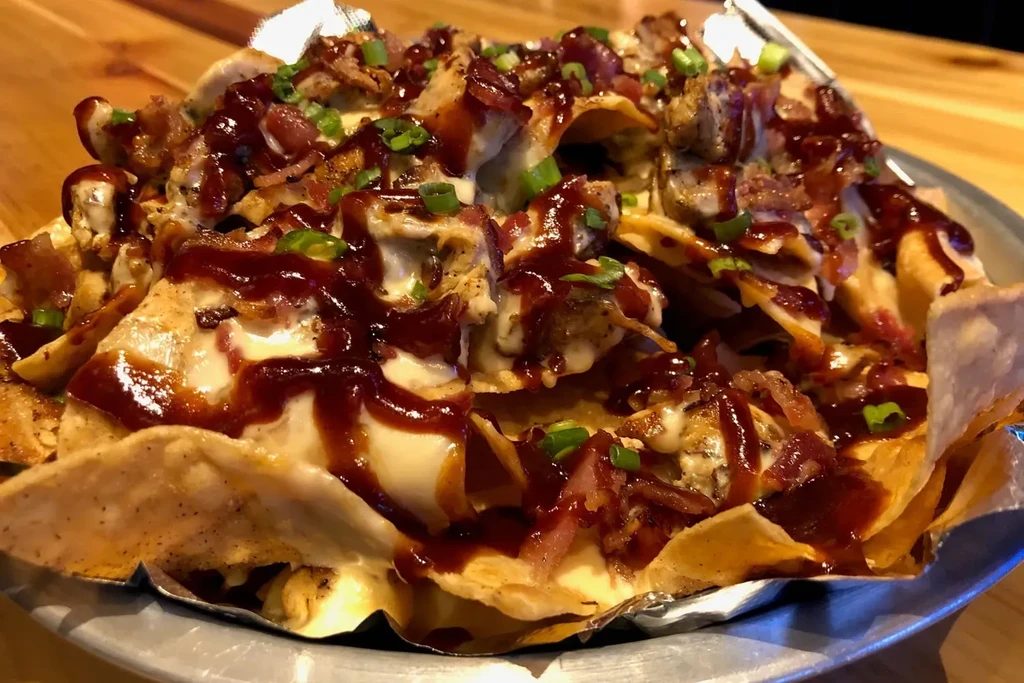 Platter of loaded nachos with cheese, chicken, bacon, BBQ, green onions.