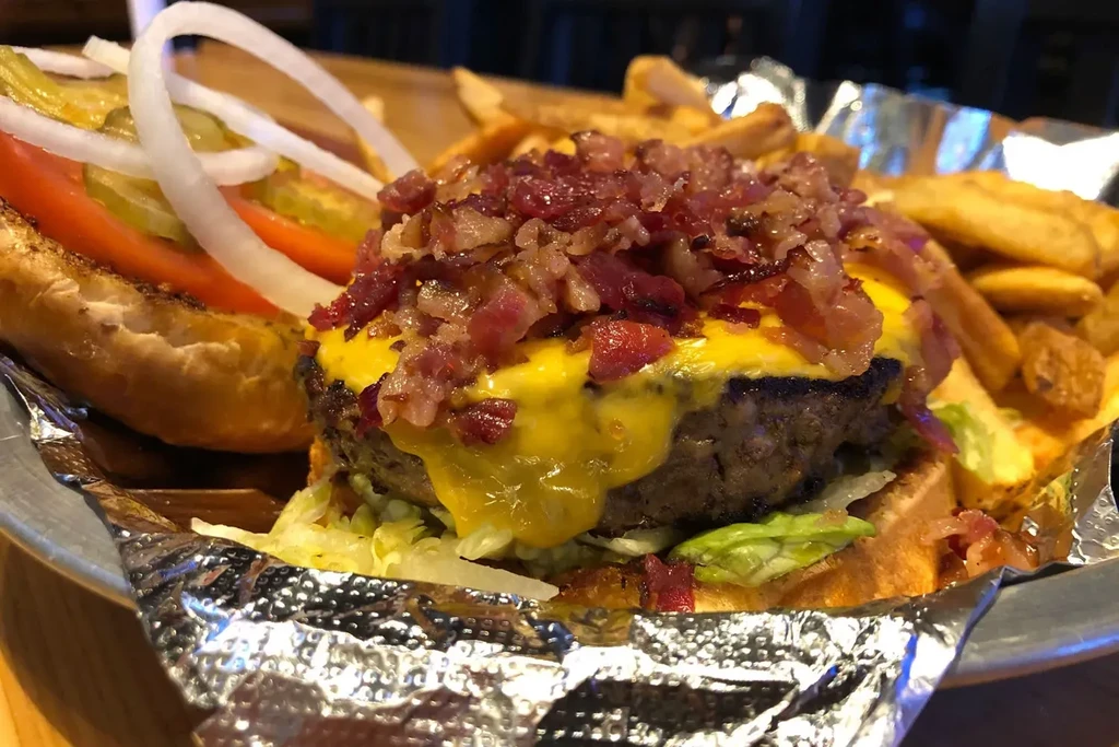 Large open-faced burger with bacon, cheese, lettuce, tomato, and fries.