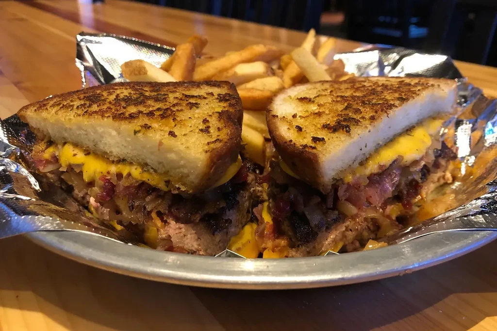 Patty melt sandwich cut in half, showing layers, with french fries.