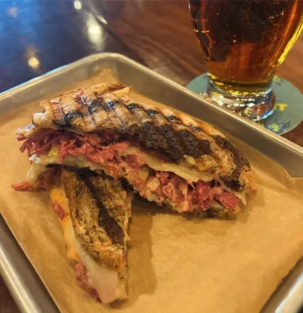 Close-up of a grilled Reuben-style sandwich and a glass of beer.