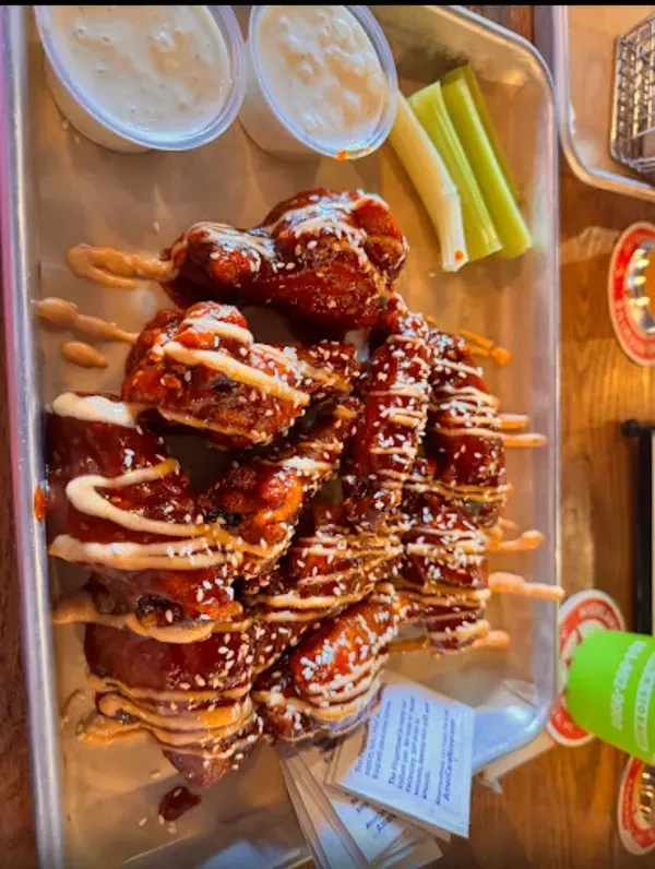Glazed chicken skewers with sesame seeds, dipping sauce, and celery sticks.