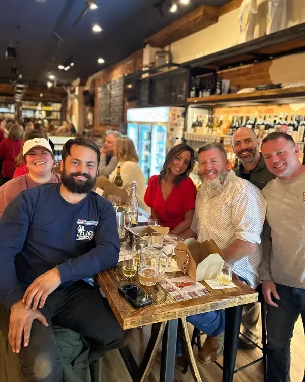 Seven smiling people around a bar table with drinks.