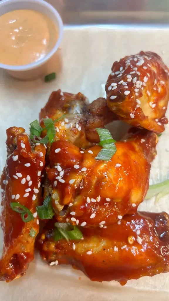 Orange-red chicken wings with sesame, green onions, and dipping sauce.