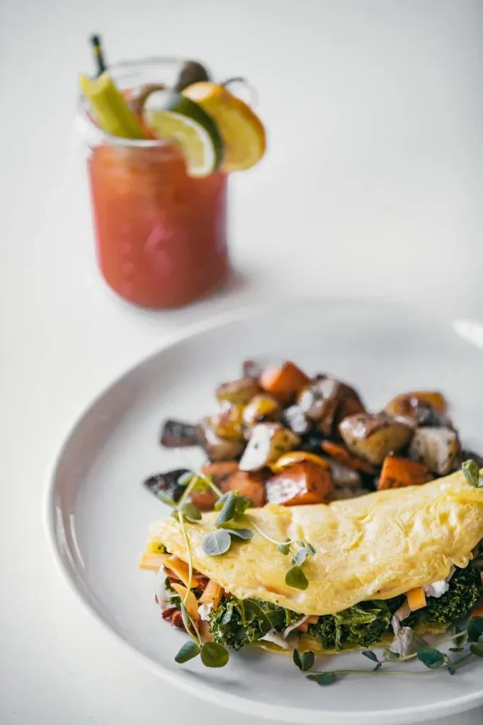 Savory omelet, roasted potatoes, and garnished reddish drink on white.