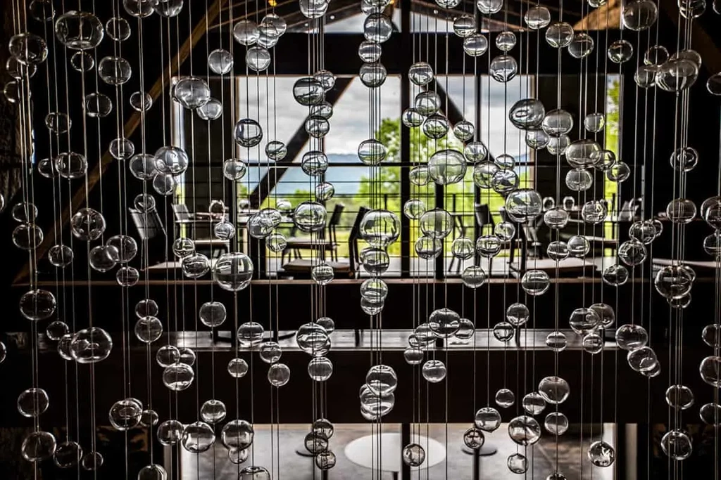 Modern dining room with suspended glass spheres and a lush landscape view.