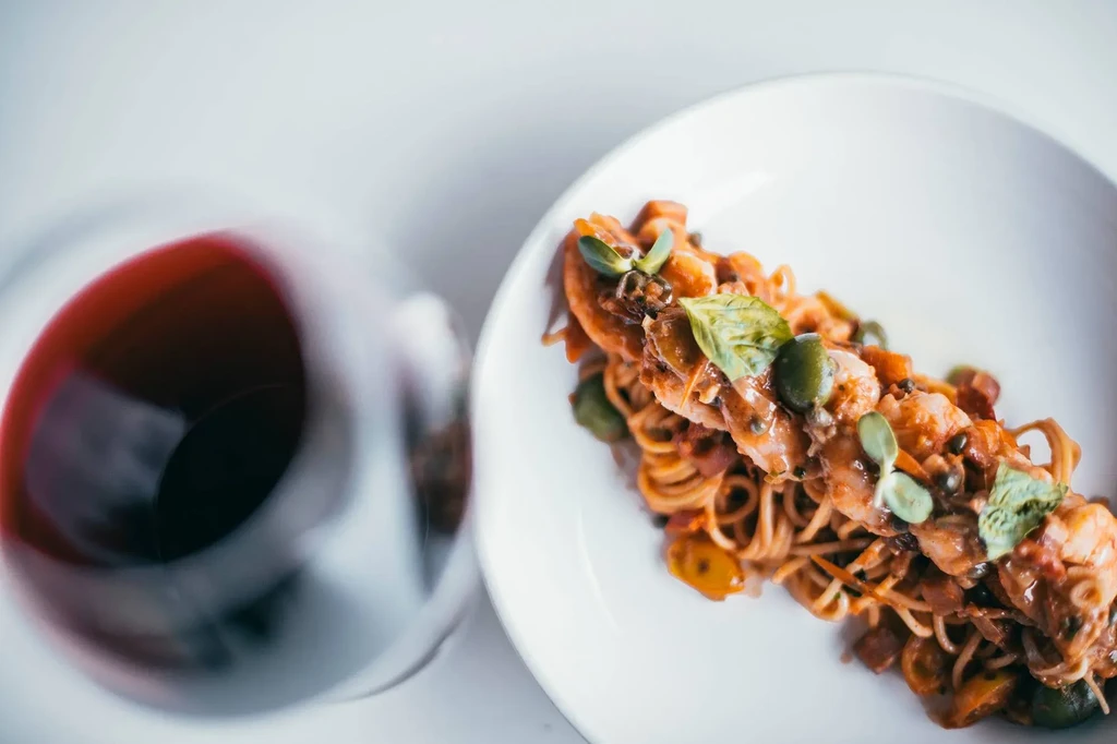 Overhead view: pasta with shrimp, red sauce, basil, and red wine.