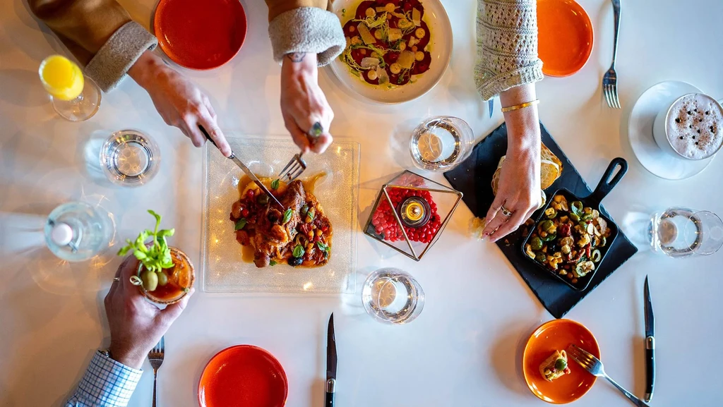 Overhead shot: hands sharing diverse, vibrant dishes and drinks.