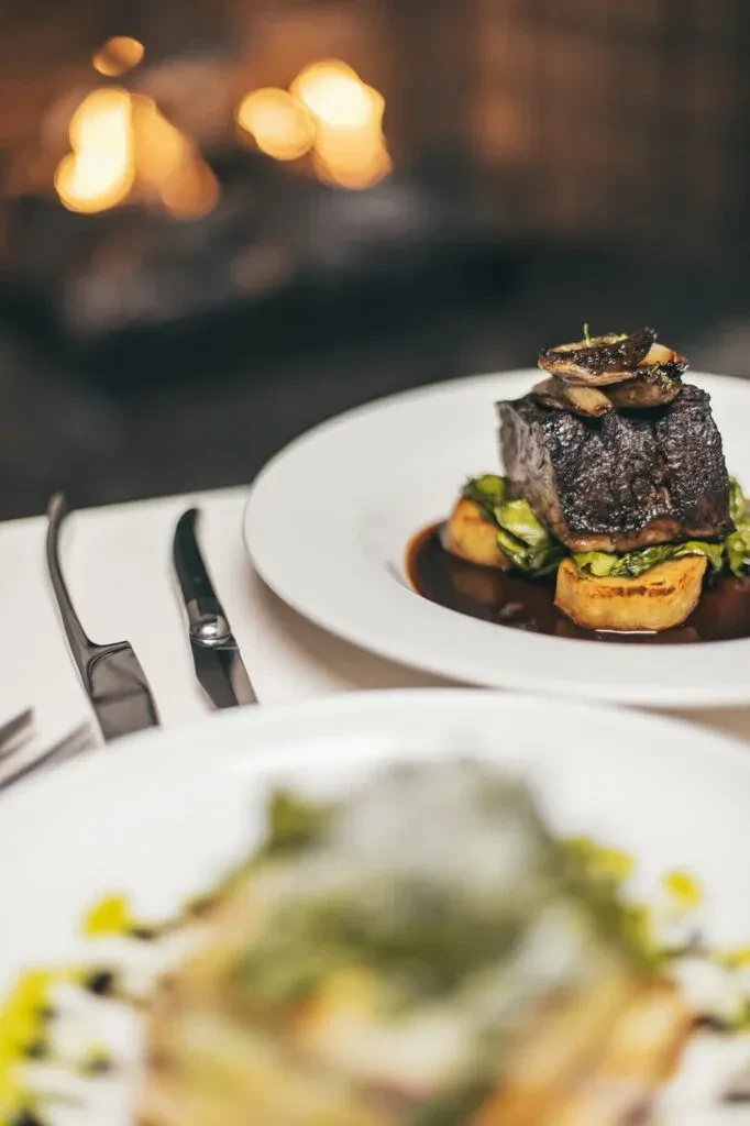 Beef short rib plate with mushrooms and potatoes on restaurant table.