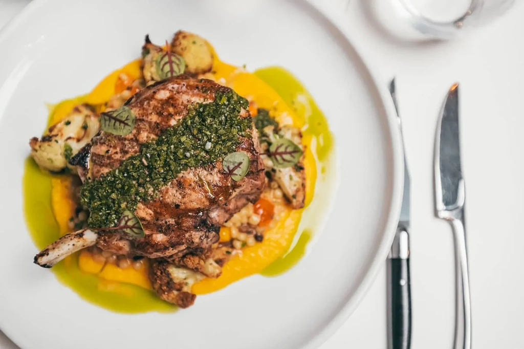 Grilled bone-in chop with green herb sauce, orange purée, and vegetables.