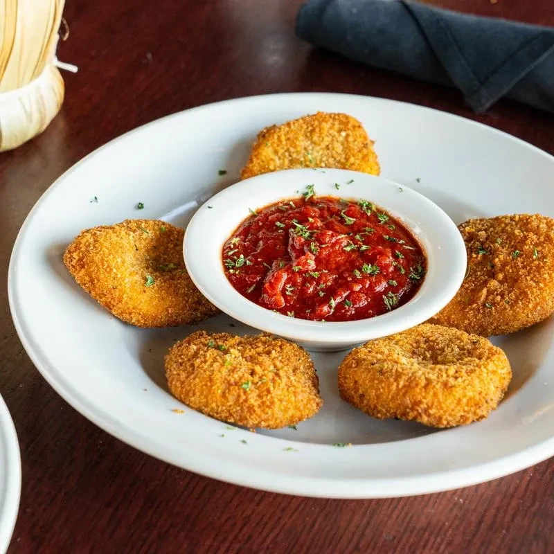 Fried mozzarella sticks arranged around marinara sauce on a white plate.