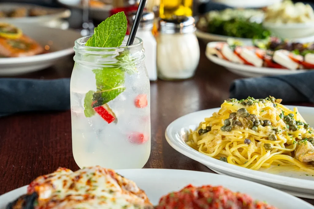 Mason jar drink and creamy pasta with capers at a restaurant table.
