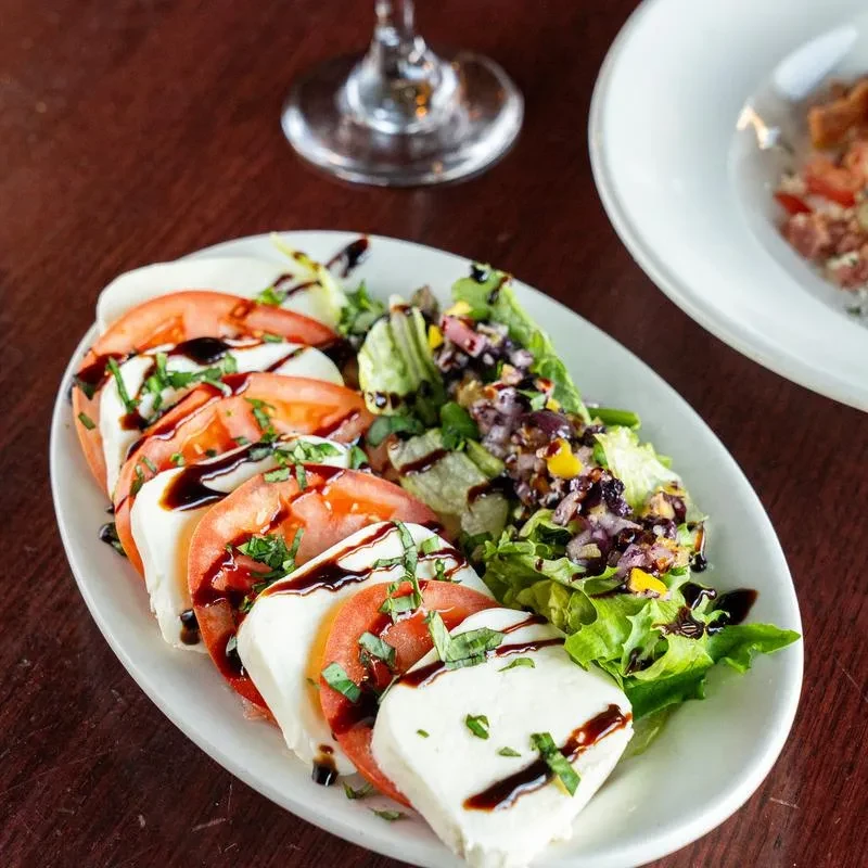 Caprese salad with side greens on a dark wooden table.