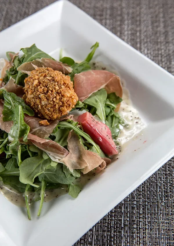 Vibrant salad with fried cheese ball, prosciutto, and leafy greens.