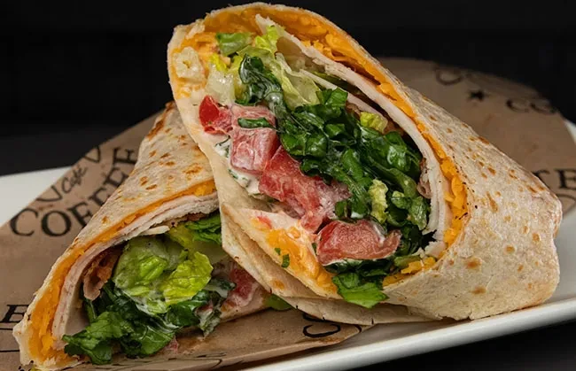 Halved tortilla wrap with lettuce, tomato, cheese, and creamy sauce.